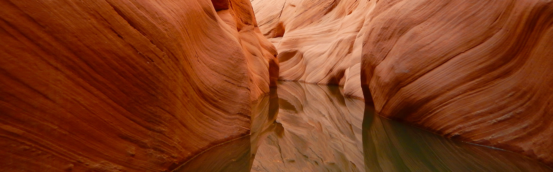 Curving orange sandstone walls above still canyon water